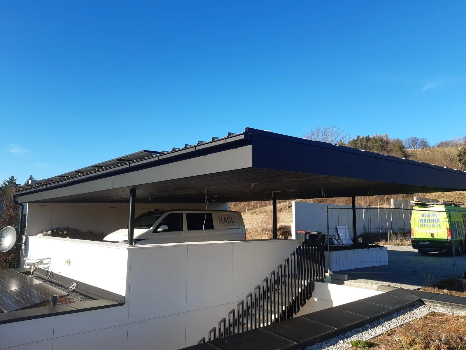 Flachdach über einem Carport an einem weißen Haus, rechts ein grüner Firmenwagen von Holzbau Wallner