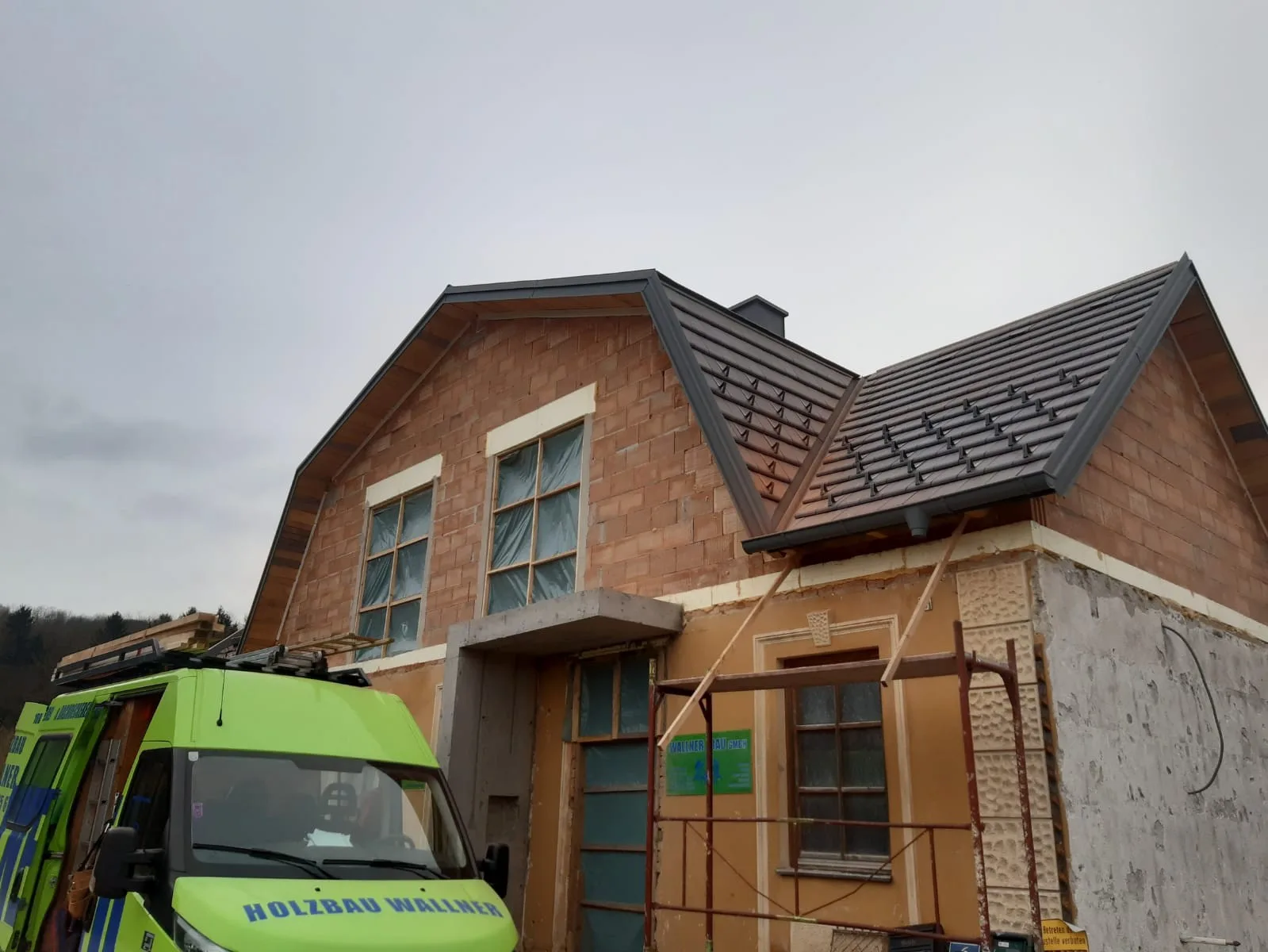 Rohbau mit neu gedecktem Mansarddach, davor ein grüner Firmenwagen mit der Aufschrift Holzbau Wallner