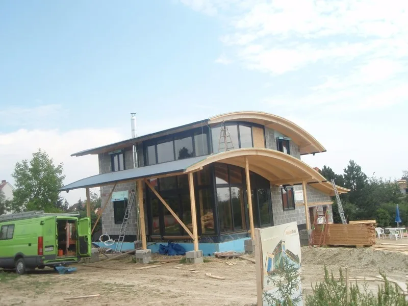 Haus mit gewölbtem Dach im Bau, davor ein grüner Firmenwagen