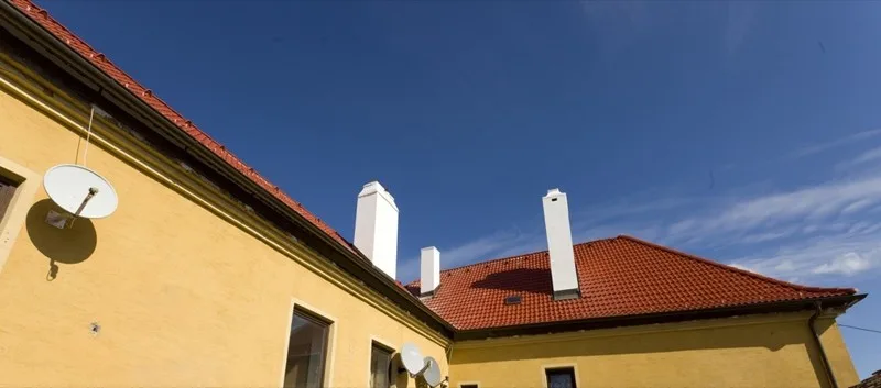 Gelbes Haus mit rotem Ziegeldach und weißen Kaminen vor blauem Himmel